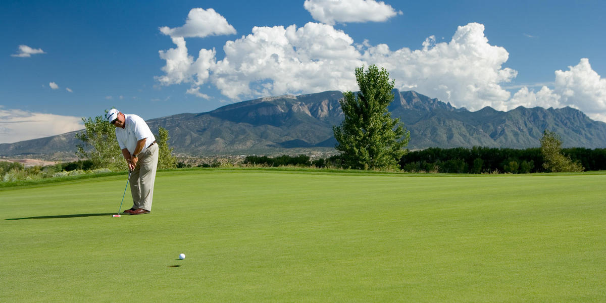 Man hitting golf ball on golf course with Sandia Mountains in background