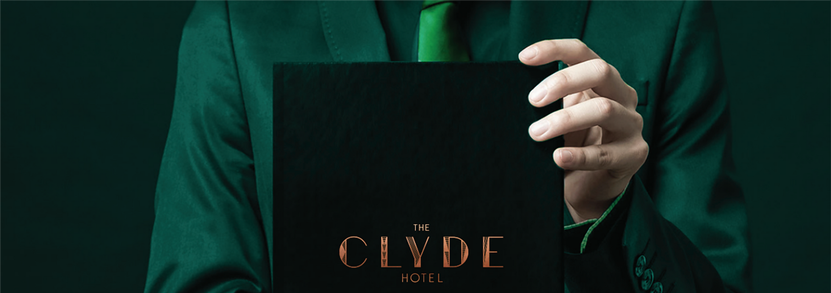 Man in green suite with hand holding book embossed with The Clyde Hotel logo