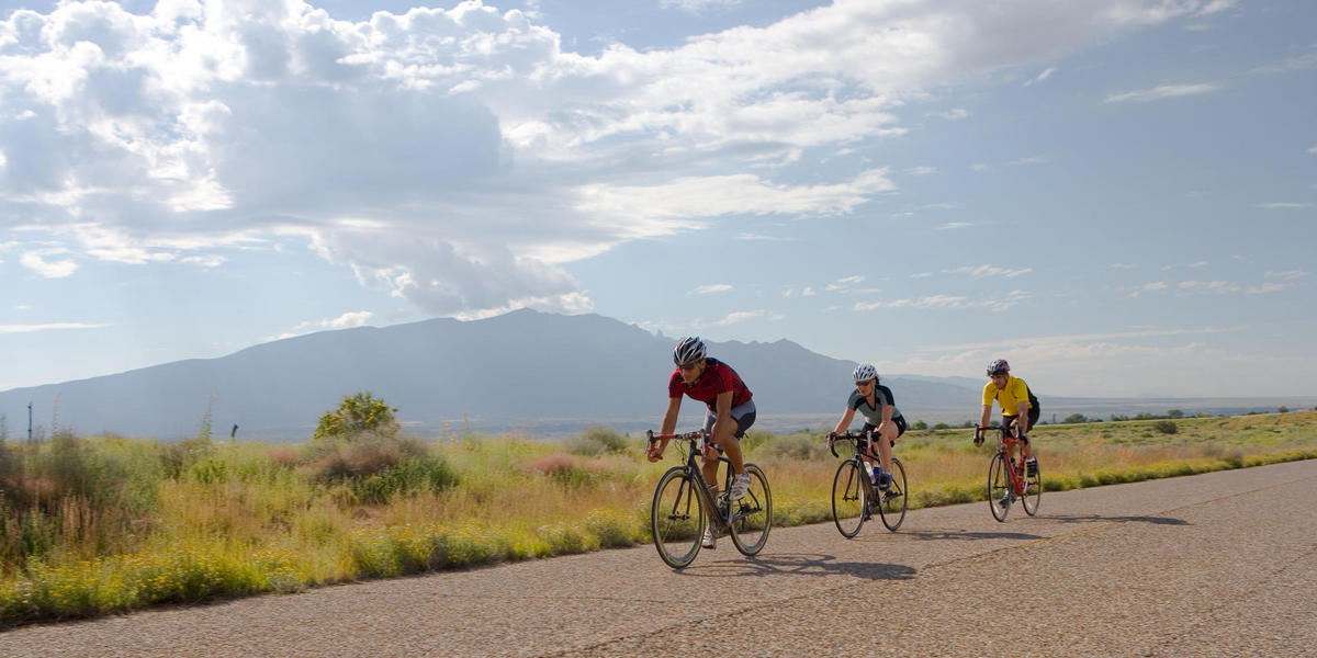 three bicyclists riding on paved trail with mountains in background